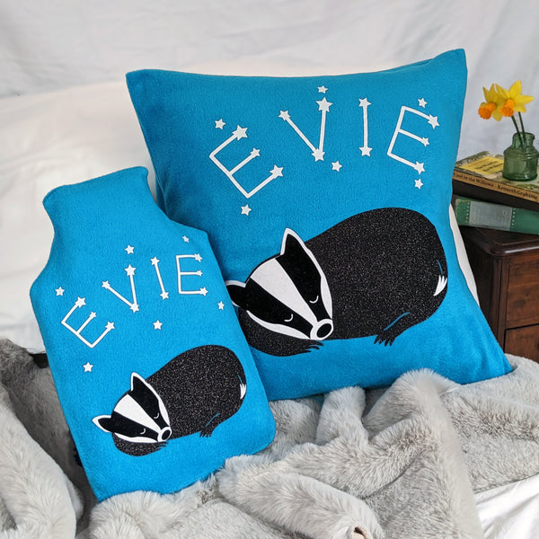 A cosy cushion and hot water bottle cover with a whimsical badger design, featuring constellations and stars. The turquoise fleece adds a pop of color to any room, making it perfect for snuggling up on cool nights