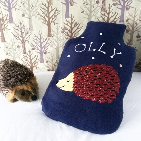 A snuggly navy fleece hot water bottle cover with a cute sleeping hedgehog design and personalized glow-in-the-dark star constellation spelling out a child's name.