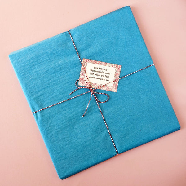 Image of a wrapped print. A square print wrapped in turquoise tissue paper with red and white twine and a floral gift note.