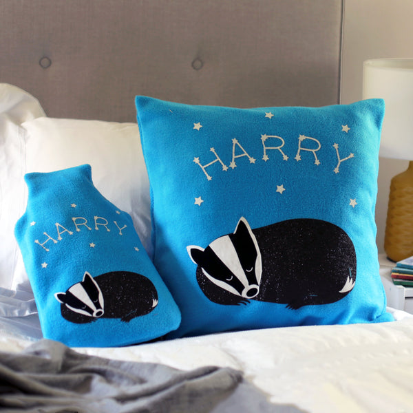 A snuggly fleece cushion and hot water bottle cover featuring a sleeping badger with a name surrounded by constellations and stars. The cushion is perfect for chilly evenings.