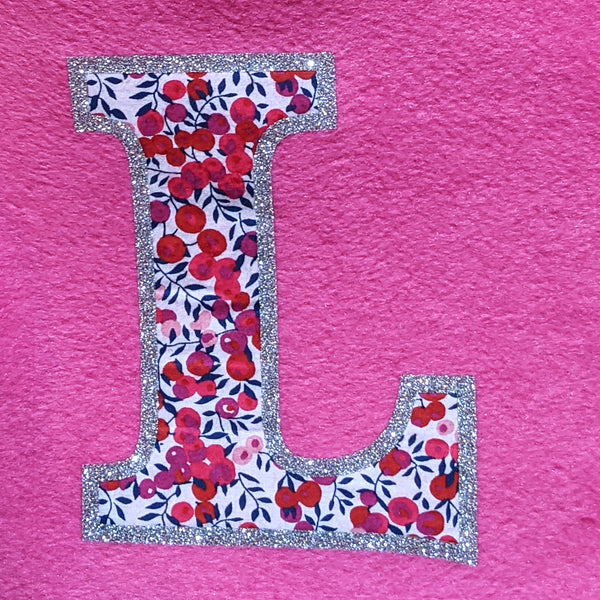 Detail of Liberty fabric initial edged with silver glitter on bright pink fleece