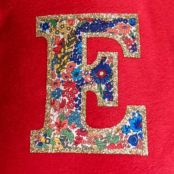 Detail of Liberty fabric initial edged with gold glitter on red fleece