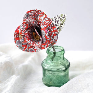 A rose made from red Liberty fabric with white flowers in a green glass bottle in 