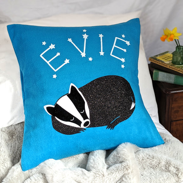 A comfortable cushion with a cute badger design. The badger is sleeping soundly amidst a starry night sky of constellations and twinkling stars.