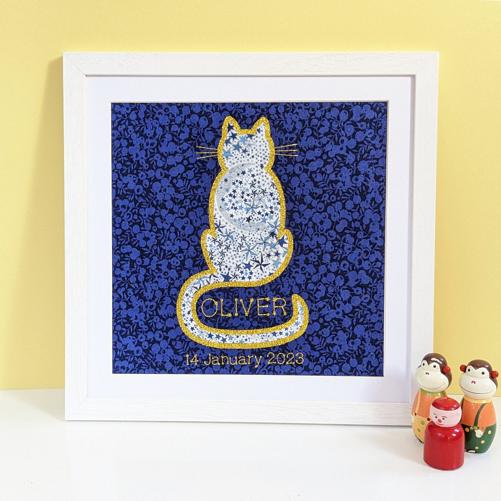 A square print showing a starry Liberty fabric cat edged with gold glitter featuring the name in the curve of the tail and date of birth below.