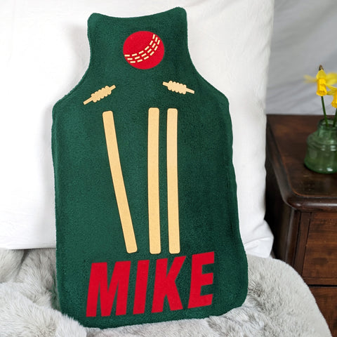 Dark green fleece hot water bottle cover with cricket stumps and ball and name in red flock.