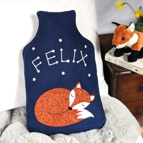 A cosy hot water bottle cover with a sleeping fox design, adorned with constellation stars spelling out a child's name in the dark.