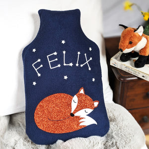 A navy fleece hot water bottle cover featuring a sleeping fox with glowing star constellations spelling out a child's name.