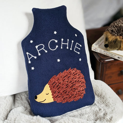 A navy fleece hot water bottle cover featuring a sleeping hedgehog with personalized glow-in-the-dark star constellations spelling out a child's name.