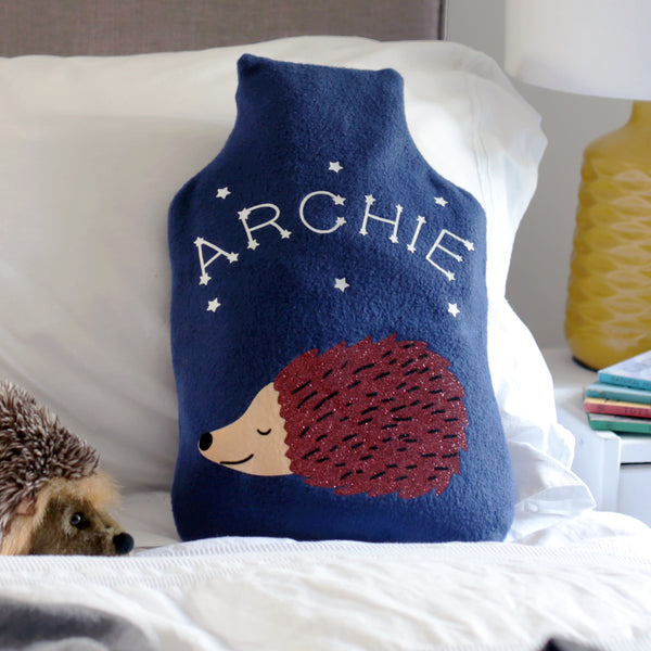 A cosy hot water bottle cover with a sleeping hedgehog design, adorned with constellation stars spelling out a child's name in the dark.
