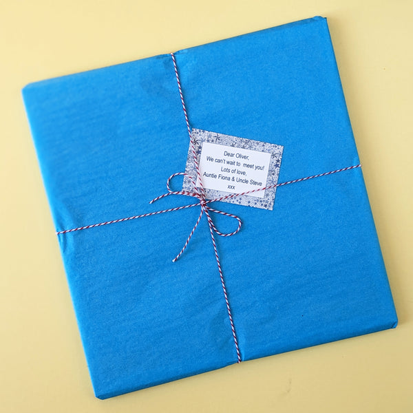 A framed print wrapped in turquoise tissue, tied with red and white twine and with a starry gift note.